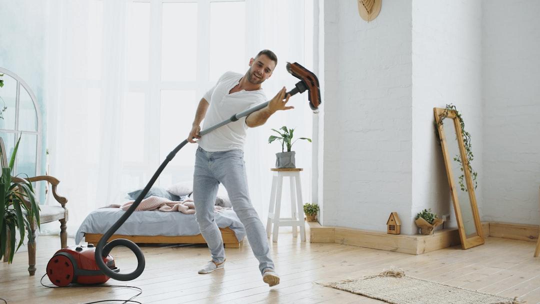 Man energetically vacuuming and dancing in a bright room.