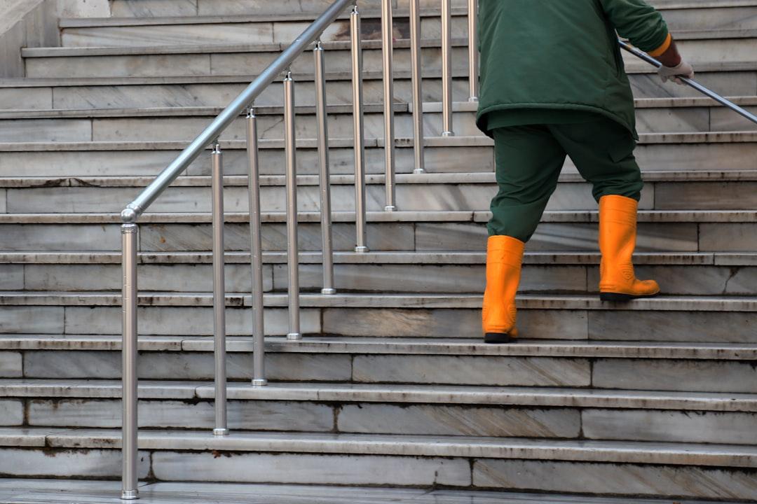 person in green jacket and brown pants walking on gray concrete stairs