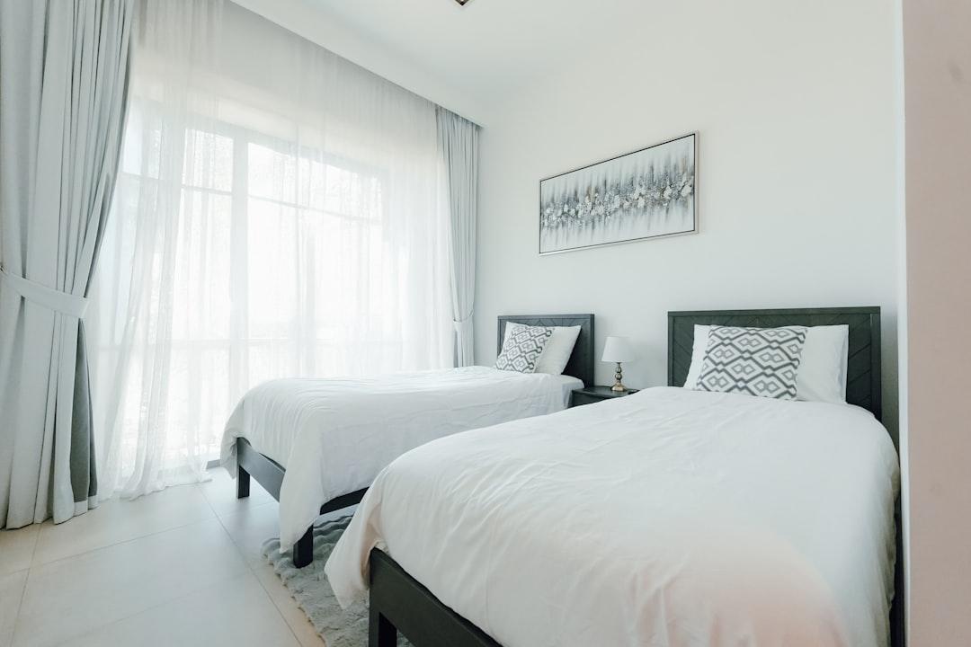 Two beds in a bright, modern bedroom with large windows.